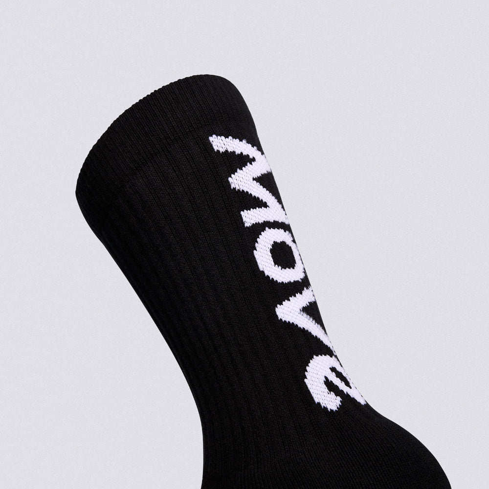 A close-up of a black ribbed crew sock with bold white 'MOW' lettering knitted vertically onto the side, set against a solid light gray background.