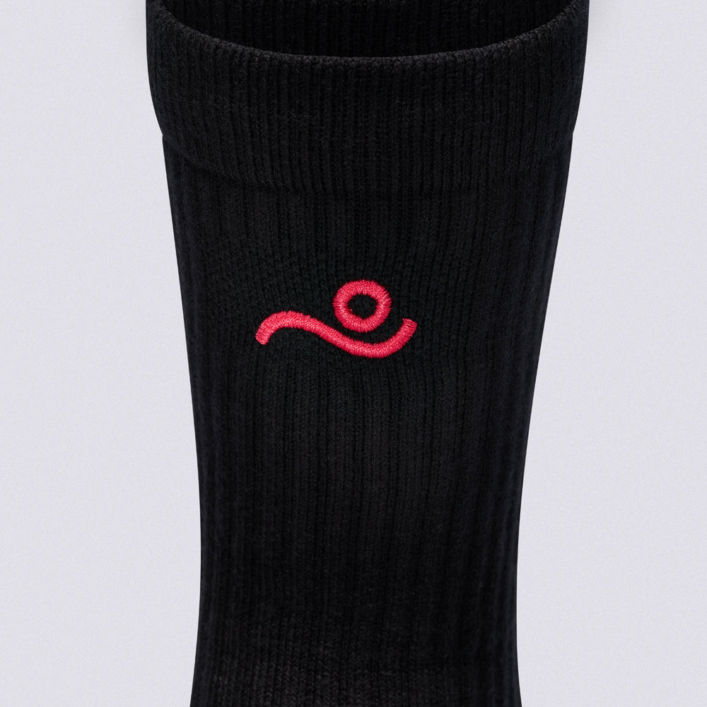 A close-up of a black ribbed athletic sock featuring a small red embroidered logo on the side, set against a plain light gray background.