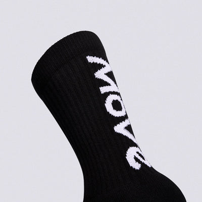 A close-up of a black ribbed crew sock with bold white 'MOW' lettering knitted vertically onto the side, set against a solid light gray background.