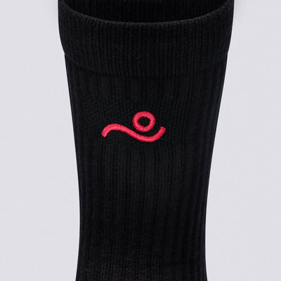 A close-up of a black ribbed athletic sock featuring a small red embroidered logo on the side, set against a plain light gray background.